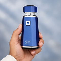 French Avenue Azzure Aoud 100 ml: Hand holding the blue bottle with silver trim against a pale blue background