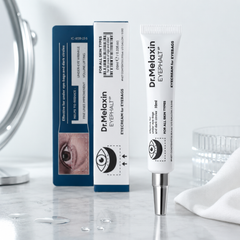 Dr. Melaxin Eyefalt eye cream in a white squeeze tube with a silver cap, standing next to its blue and white packaging box on a light marble surface.
